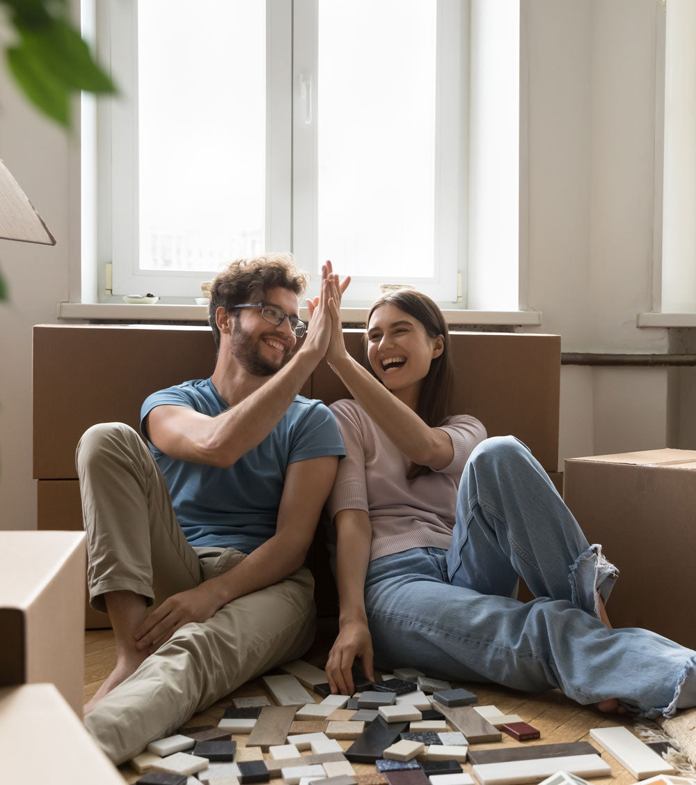 Couple high fiving while sitting in a living room looking at tile samples on the floor 